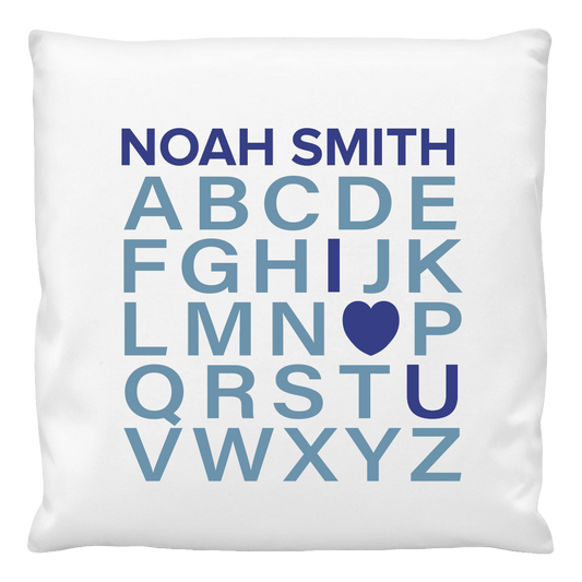 A white cushion cover with the text 'NOAH SMITH' and the alphabet from 'A' to 'Z', with a heart symbol replacing the letter 'I', printed in blue.