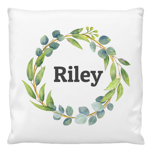 A white cushion cover with the name 'Riley' printed in the center, surrounded by a leafy wreath design.