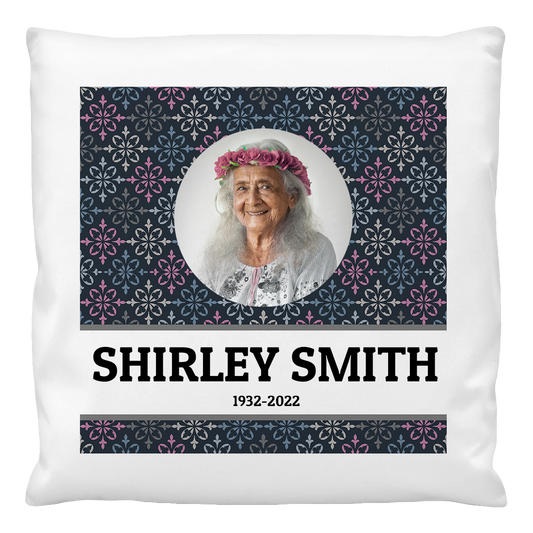 A cushion cover featuring a printed photo of an older woman with a floral pattern in the background. The name 'SHIRLEY SMITH' and the years '1932-2022' are printed on the cushion.